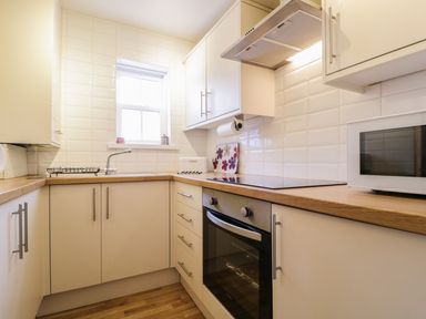 A kitchen with white cabinets a wooden countertop an oven a stove a microwave and a window at Siskin Keswick