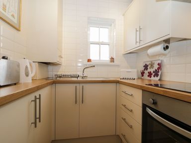 A small kitchen with white cabinets wooden countertops a toaster kettle oven and a window at Siskin in Keswick
