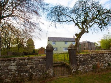 A stone wall with a gate leading to a yard with a green house a wooden shed and a stone building at Westmains Farm in Penton