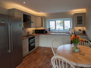 A kitchen with white cabinets wooden floor and a round table with flowers at Westmains Farm in Penton