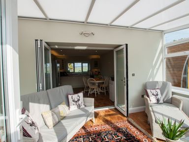 A sunroom with wicker furniture and cushions next to a dining area with table and chairs at Westmains Farm in Penton