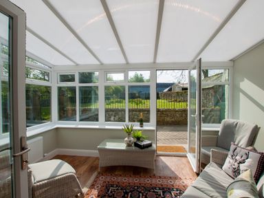 A sunroom with wicker furniture a glass table plants and a bottle outside at Westmains Farm in Penton