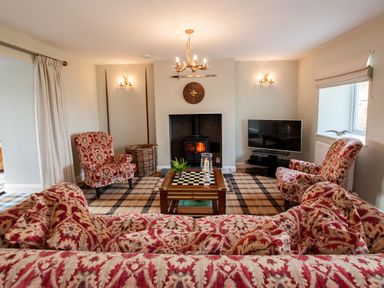 A living room with patterned armchairs and sofa a coffee table a fireplace and a television at Westmains Farm in Penton