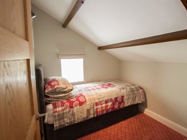 A bedroom with a single bed covered with a patchwork quilt under a slanted ceiling with exposed beams at Westmains Farm in Penton