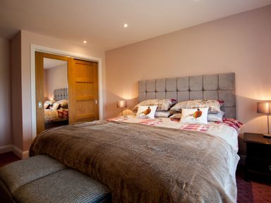 A bedroom with a bed with a padded headboard two bedside tables with lamps and a sliding door wardrobe at Westmains Farm in Penton