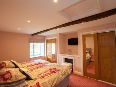 A bedroom with two beds a window wooden sliding doors a mounted television and a vanity area at Westmains Farm in Penton