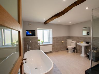 A bathroom with a bathtub toilet sink window and wooden ceiling beam at Westmains Farm in Penton