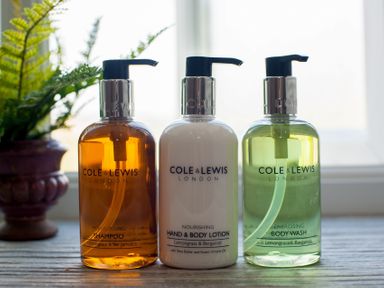Three pump bottles of Cole Lewis shampoo hand and body lotion and body wash on a wooden surface with a plant in a pot in the background at Westmains Farm in Penton