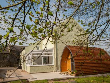 A house with a conservatory and a wooden pod outside with branches and leaves in foreground at Westmains Farm in Penton