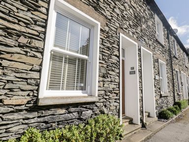Stone exterior of a house with windows doors and small plants along the wall at Raglan Cottage in Bowness-on-Windermere