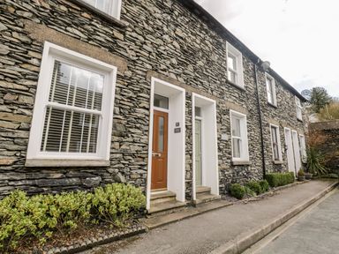 A stone exterior terrace with multiple doors and windows along a narrow street at Raglan Cottage in Bowness-on-Windermere