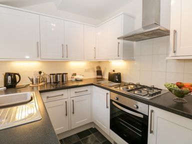 A kitchen with white cabinets black countertop a gas stove a toaster and a fruit bowl at Raglan Cottage in Bowness-on-Windermere
