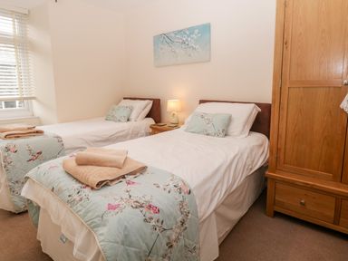 A bedroom with two single beds a bedside table lamp wooden wardrobe and a window at Raglan Cottage in Bowness-on-WIndermere