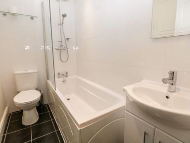 A bathroom with a toilet bathtub with shower and a sink with cabinet at Raglan Cottage in Bowness-on-Windermere