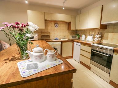 A kitchen with wooden countertops flowers in a glass vase and a teapot on a tray at Treetops in Windermere