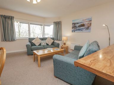 A living room with two sofas and a wooden coffee table with cushions on the sofas at Treetops in Windermere