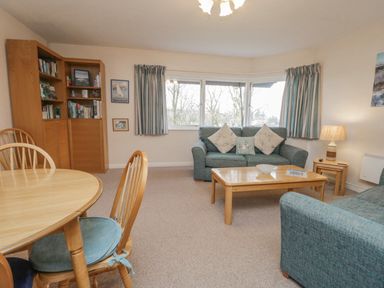 A living room with blue sofas a wooden coffee table and dining table with chairs at Treetops in Windermere