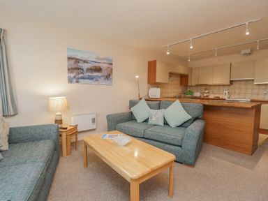 A living room with sofas pillows and a wooden coffee table next to a kitchen with cabinets at Treetops in Windermere