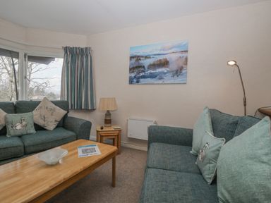 A living room with two sofas a wooden coffee table a lamp and wall art at Treetops in Windermere