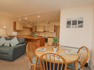 An open kitchen and dining area with a wooden table, four chairs, a grey sofa, and kitchen cabinets at Treetops in Windermere