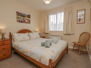 A bedroom with a wooden double bed and bedside tables with lamps at Treetops in Windermere