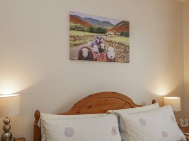 A bedroom with a wooden headboard two pillows two bedside lamps and a painting of sheep on the wall at Treetops in Windermere