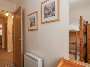 A hallway with two framed pictures on the wall a wooden door open a heater and a bunk bed reflected in a mirror at Treetops in Windermere