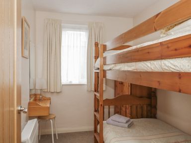 A small bedroom with wooden bunk beds a side table with lamp and stool under a window at Treetops in Windermere
