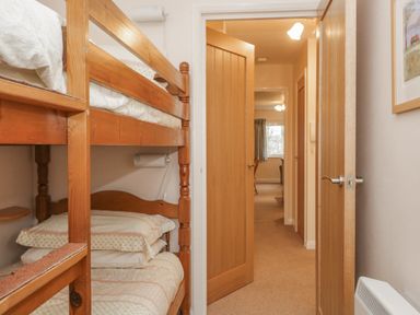 A small bedroom with wooden bunk beds and an open door leading to a hallway at Treetops in Windermere