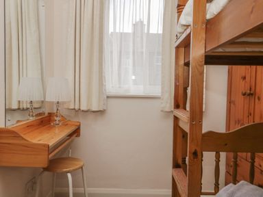 A small room with a wooden bunk bed wooden desk with a lamp stool and window with curtains at Treetops in Windermere