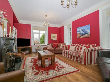 A living room with red walls striped and leather sofas wooden coffee table rug and fireplace at The Old Vicarage in Keswick