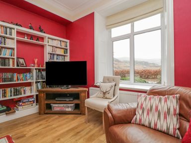 A corner living room with a window a television on a wooden stand bookshelves and two chairs at The Old Vicarage in Keswick