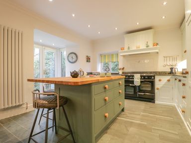 A kitchen with an island, bar stools, a stove, and cabinets at The Old Vicarage in Keswick