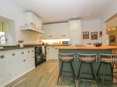 A kitchen with white cabinets a black stove and an island with stools at The Old Vicarage in Keswick
