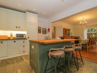 A kitchen with green island and three bar stools next to a dining area with wooden chairs and table at The Old Vicarage in Keswick