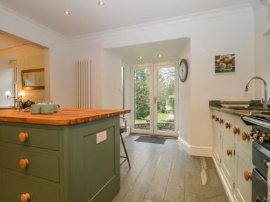 A kitchen with an island and wooden countertop near glass doors leading to a garden at The Old Vicarage in Keswick