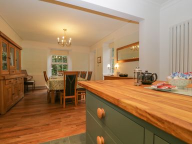 A kitchen island with tea set and snacks and a dining table with chairs and wooden cabinet in the background at The Old Vicarage in Keswick