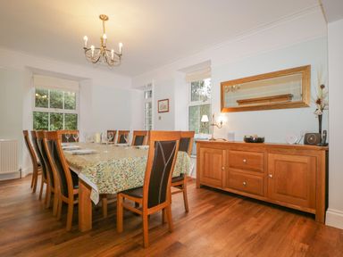 A dining room with a wooden table covered with patterned cloth and chairs around it at The Old Vicarage in Keswick