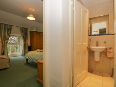 A bedroom with green carpet and wooden furniture next to a bathroom with a sink and mirror at The Old Vicarage in Keswick