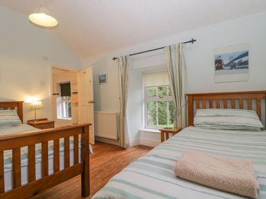 A bedroom with two single beds a window with curtains a bedside table and an open door at The Old Vicarage in Keswick