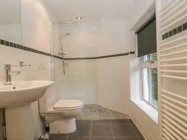 A bathroom with a toilet sink shower with glass partition and window with blind at The Old Vicarage in Keswick