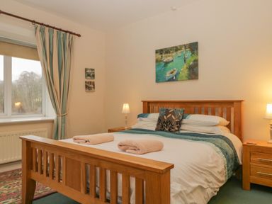 A bedroom with a wooden bed two bedside tables with lamps and a window with striped curtains at The Old Vicarage in Keswick