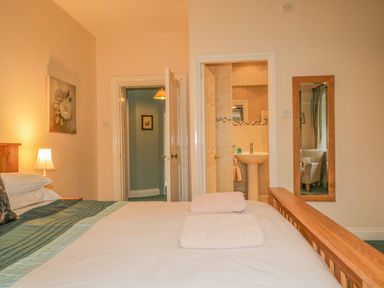 A bedroom with a bed with folded towels a bedside lamp and a door leading to a bathroom at The Old Vicarage in Keswick