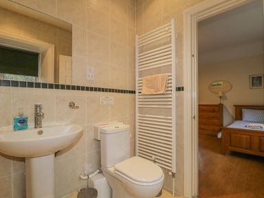 A bathroom with a sink toilet and towel rail next to a bedroom with a bed and wooden dresser at The Old Vicarage in Keswick