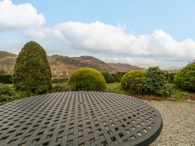 A metal outdoor table on a gravel surface with bushes and hills in the background at The Old Vicarage in Keswick