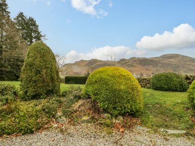 A garden with trimmed bushes gravel and mountains in the background at The Old Vicarage in Keswick