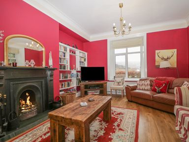 A living room with a wooden coffee table a fireplace bookshelf and a brown leather sofa at The Old Vicarage in Keswick
