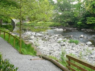 A gravel river path with wooden fencing and a tree beside a rocky river at 5 Keswick Bridge in Keswick