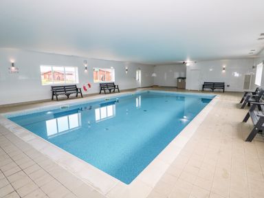 An indoor swimming pool with benches along the walls and windows showing outside cabins at Ash Lodge in Greetham Rutland