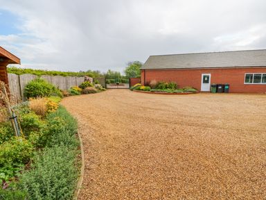 A gravel driveway with planting beds along wooden fence and a brick building at Ash Lodge in Greetham Rutland